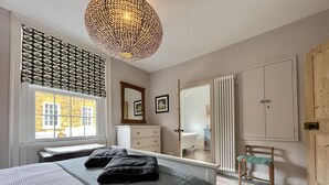 A bedroom with a bed, a dresser, a chair, a radiator, and a window with a view of a building.