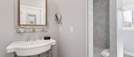 A bathroom with a white sink, a large mirror, a handheld showerhead, and a bathtub.