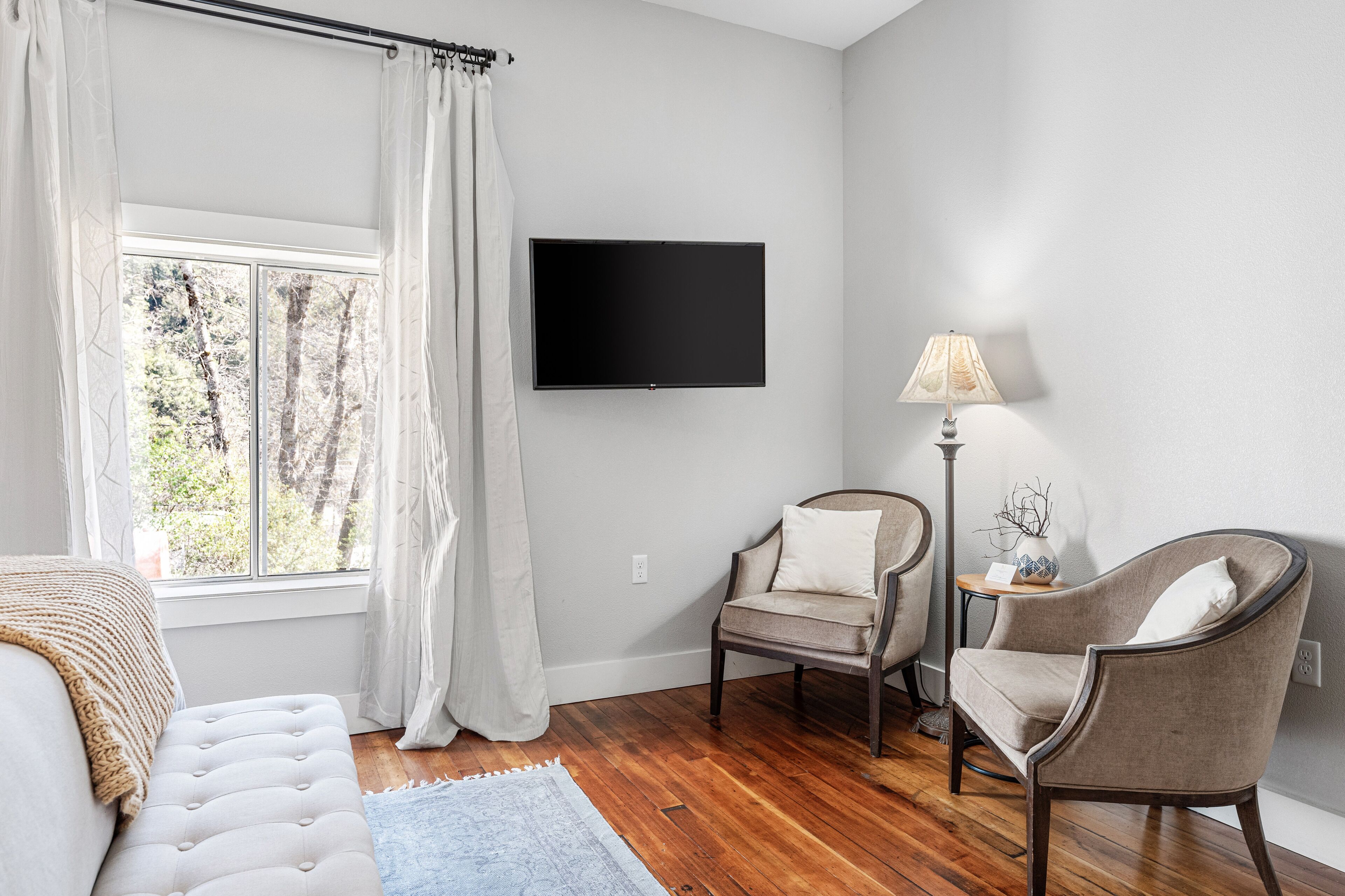 Una sala de estar moderna con un televisor de pantalla plana, dos sillones, un sofá y una mesita auxiliar con una lámpara.