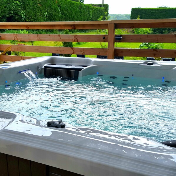 A hot tub with a wooden deck and a grassy background.