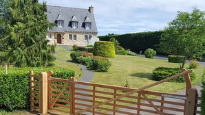 A gated entrance to a stone building with a sloped roof, surrounded by well-maintained hedges and a lawn. - L'horizon Holiday Apartment (Erquy)