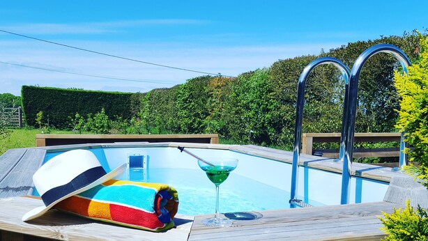 A wooden deck with a swimming pool, a lounge chair, and a glass of a green beverage. - L'horizon Holiday Apartment (Erquy)
