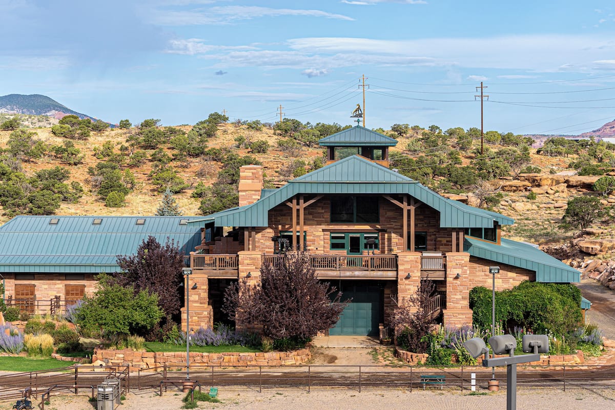 A stone building with a green roof, a balcony, and a view of a mountainous landscape.