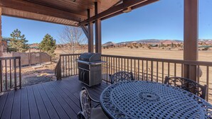 A wooden deck with a grill and metal table, overlooking a desert landscape.