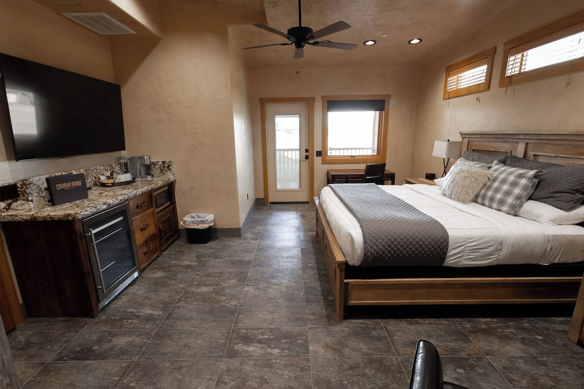 A bedroom with a bed, a desk, a TV, and a window.