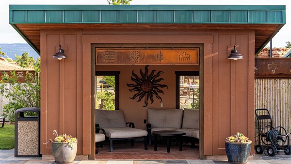 A covered outdoor seating area with two chairs and a table, a decorative sun mural, and a recycling symbol on the wall.