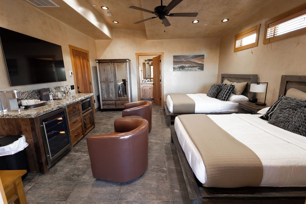A spacious hotel room with a large bed, a separate seating area, a kitchenette, and a ceiling fan.