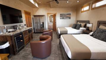 A spacious hotel room with a large bed, a separate seating area, a kitchenette, and a ceiling fan.