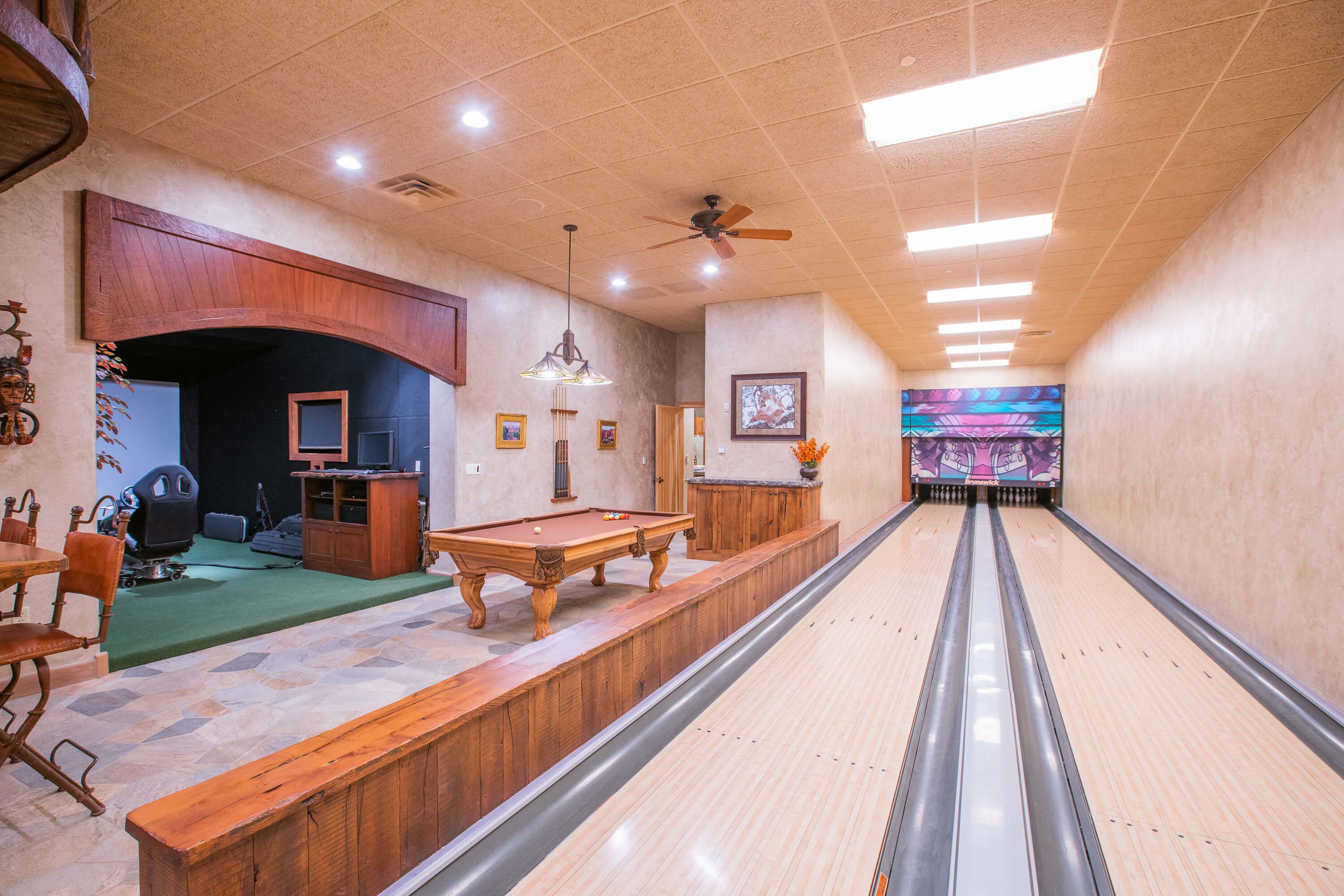 A bowling alley with a wooden pool table, a billiards table, and a bowling lane.