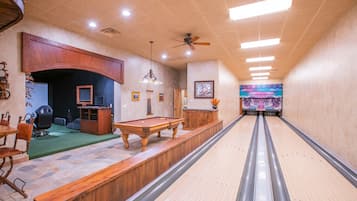 A bowling alley with a wooden pool table, a billiards table, and a bowling lane.