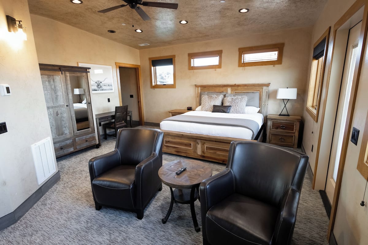 A bedroom with a bed, two chairs, a small table, a nightstand, and a ceiling fan.