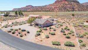 A residential area with a house surrounded by sparse vegetation and a large mountain in the background. - Midnight Manor, Kanab: red rock views, pet-ready (Kanab)