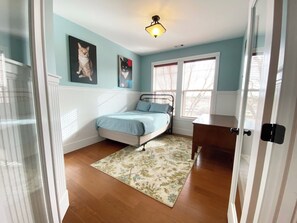 Une chambre à coucher comprenant un lit, un bureau, une fenêtre avec des stores et un luminaire au plafond.