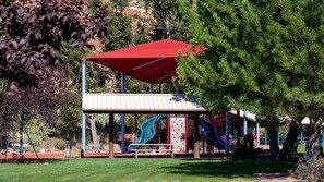 Children can play on the playground's slides and climbing elements under a shaded canopy.