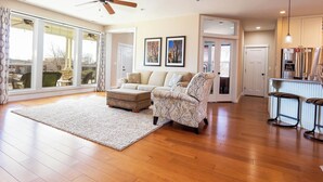 A spacious living room with a large window, a sofa, a coffee table, and a kitchen area with a refrigerator and bar stools. - Midnight Manor, Kanab: red rock views, pet-ready (Kanab)