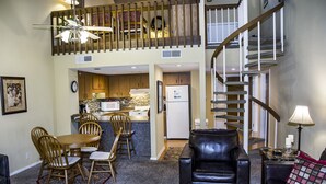 A spacious living area with a dining table, chairs, a black leather sofa, and a staircase leading to an upper level.