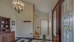 Ein Flur mit einer Holztreppe, einem Chandelier, einer Glastür und einem gemusterten Boden.
