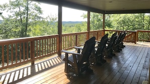 Een overdekt terras buiten, met houten leuningen en verschillende Adirondack-stoelen.