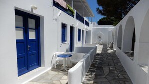 A narrow, stone-paved corridor with white walls and blue doors, leading to a small seating area with a table and chairs. - Sourmeli Pension (Mykonos)