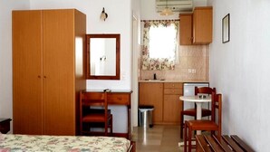 A room with a bed, a desk, a chair, a small table, and a kitchenette. - Sourmeli Pension (Mykonos)