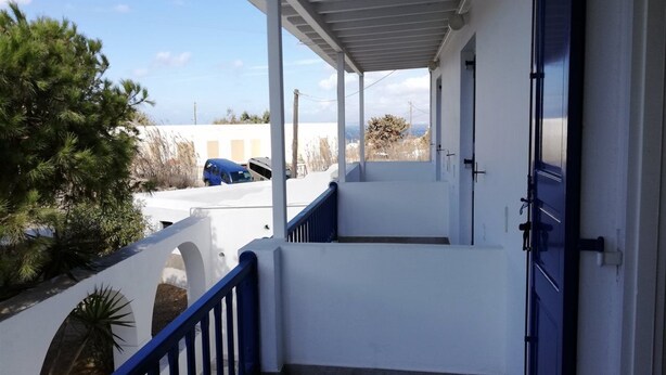 A covered outdoor area with a blue railing, a white wall, and a door. - Sourmeli Pension (Mykonos)