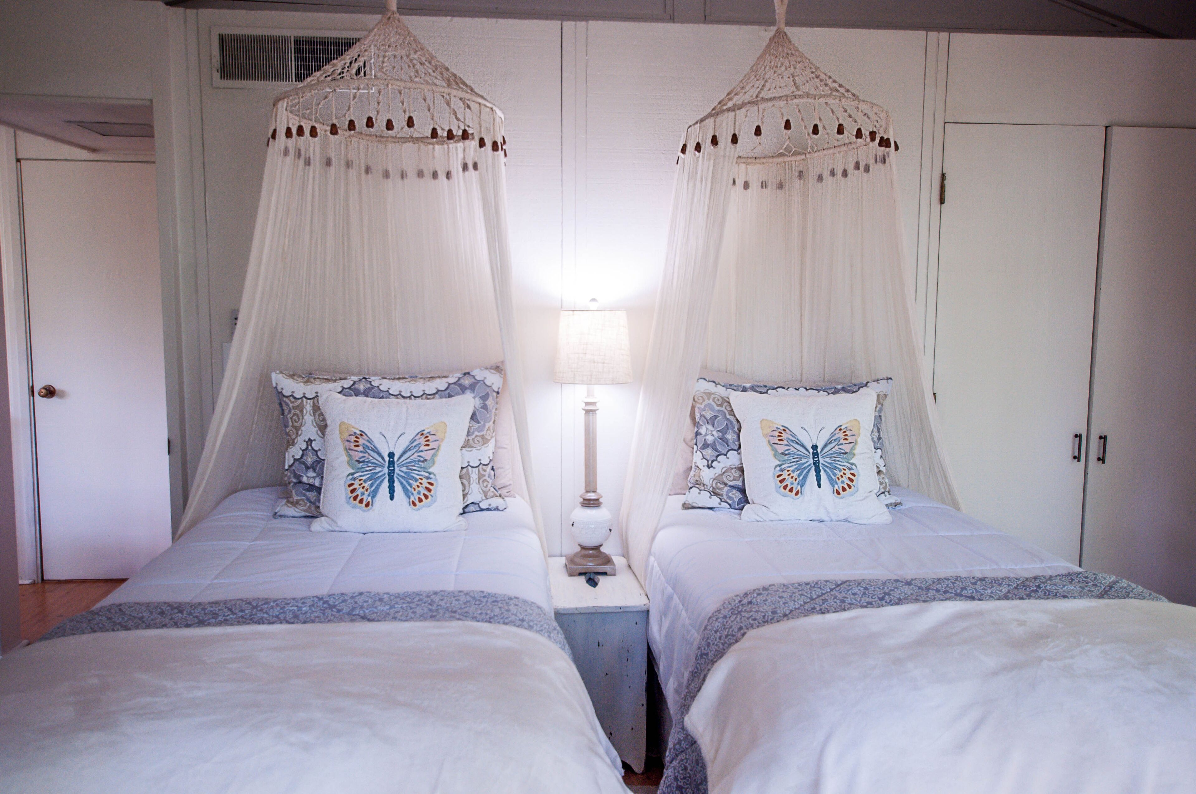 Ein Schlafzimmer mit zwei Betten, jedes mit Baldachin und Kissen mit Schmetterlingsmotiv.