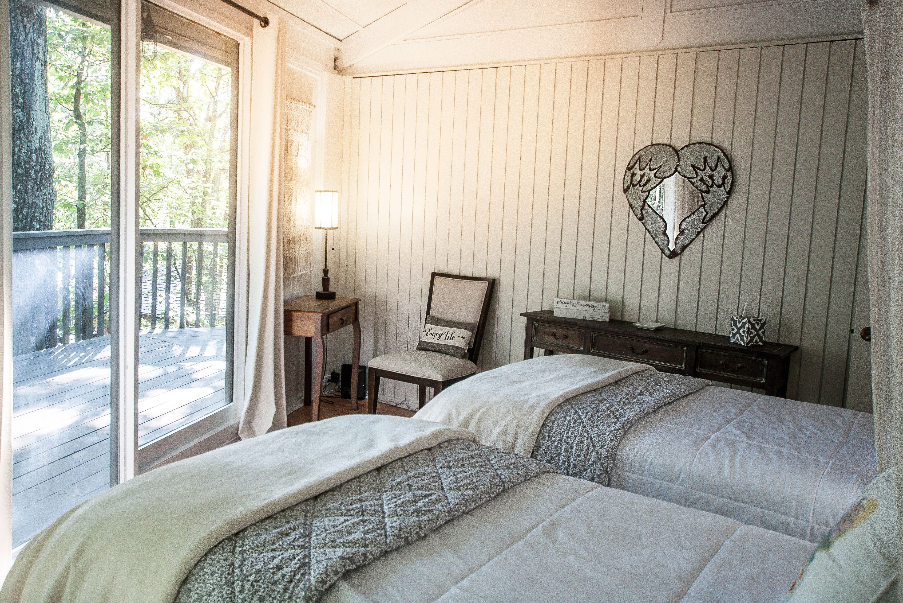 Une chambre avec un grand lit, une table de chevet, une chaise, un décor mural en forme de cœur et une vue sur l’extérieur par une fenêtre.