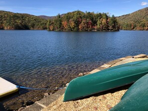 A calm lake with boats docked at a gravel dock, surrounded by forested hills.