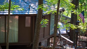 A cabin with a wooden deck, a staircase, and a view of the surrounding forest.
