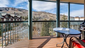 A balcony with a metal railing, a small round table, and a grill. - Centennial Studio Condo Unit 11a (Avon)