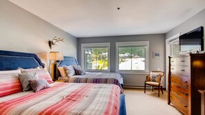 A bedroom with two beds, a dresser, a chair, and a television. - Centennial Studio Condo Unit 11a (Avon)