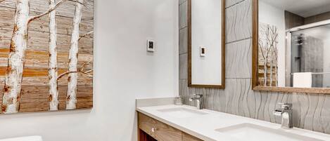 A modern bathroom with two sinks, a large mirror, and a wall-mounted artwork.