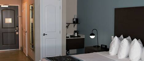 A hotel room with a bed, bedside table, lamp, and a door leading to another room.
