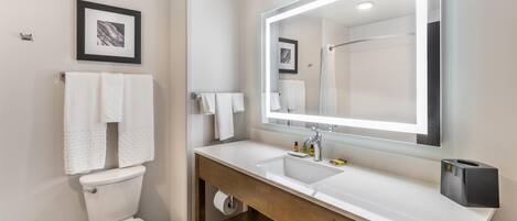 Un baño moderno con inodoro, dos lavamanos, un espejo grande y cabina de ducha.