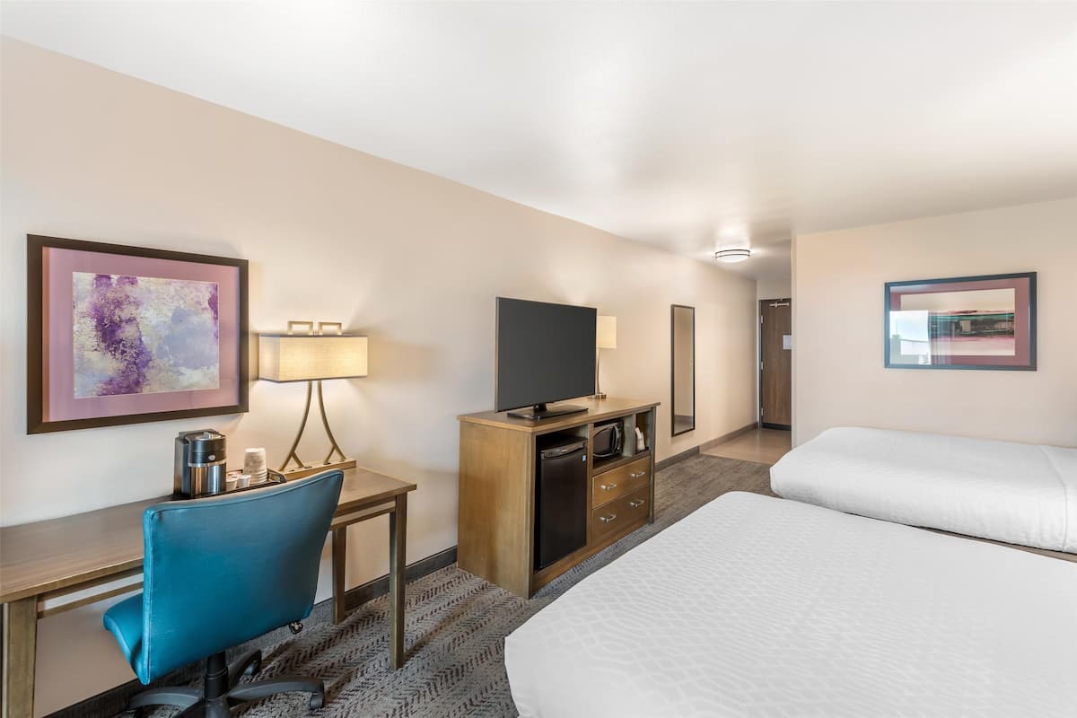 A hotel room with a desk, a chair, a television, a minibar, and two beds.