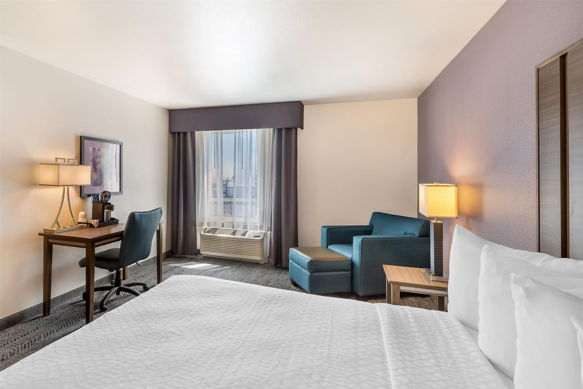 A hotel room with a large bed, a desk with a chair, a small sofa, and a window with curtains.