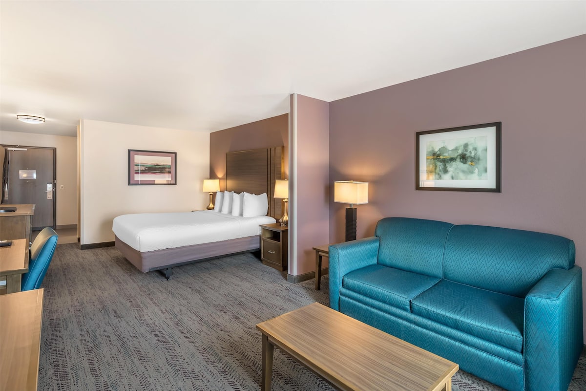 A hotel room with a bed, a blue sofa, a desk, and a chair.
