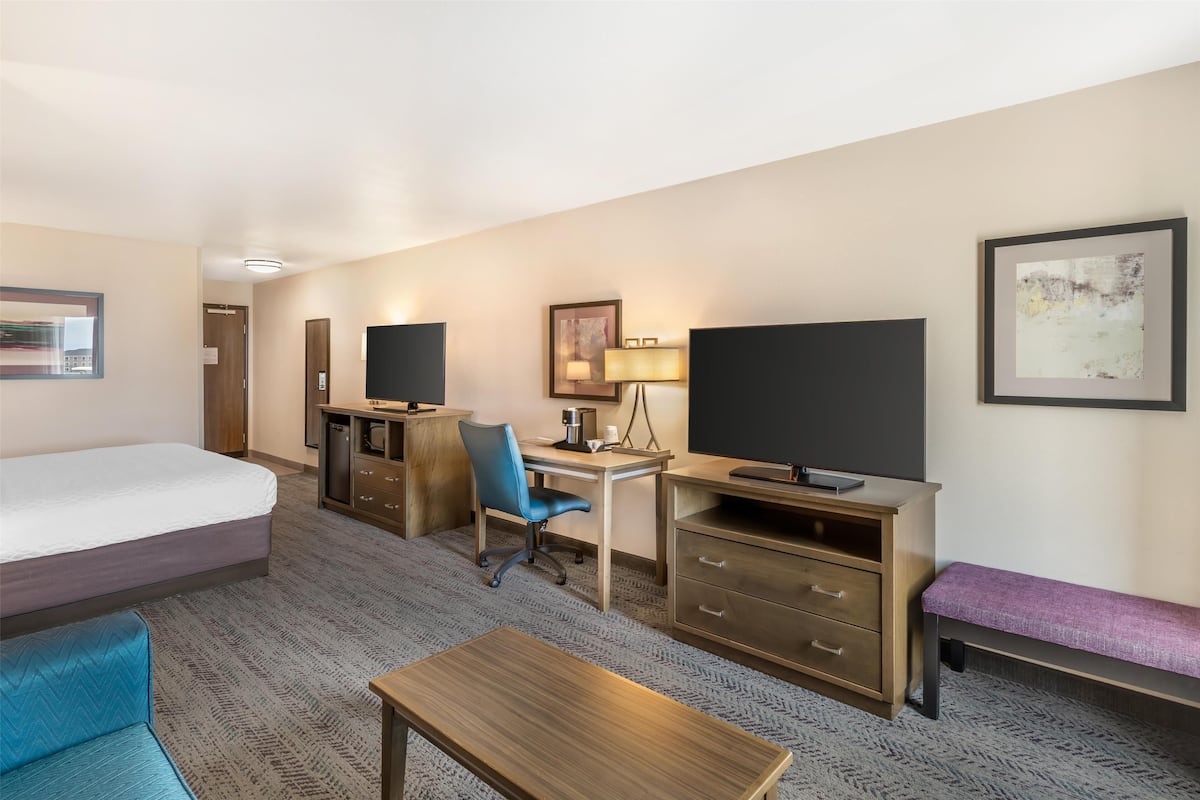 A hotel room with a bed, desk, chair, TV, and a bench.