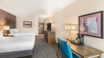 A hotel room with two beds, a desk, a chair, a TV, and a coffee maker.