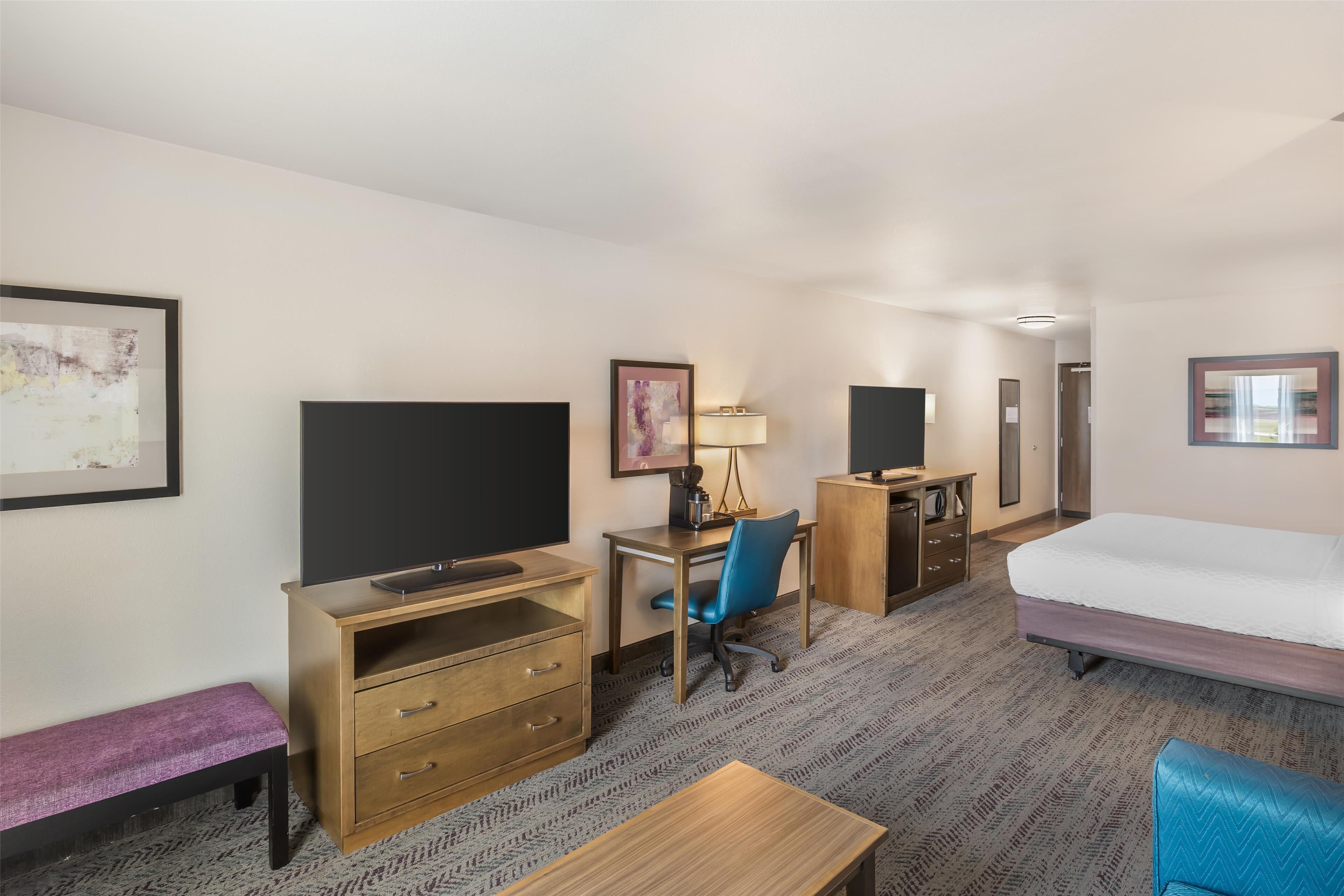 Una habitación de hotel con una cama, un escritorio con silla, una televisión, un aparador y un banco.