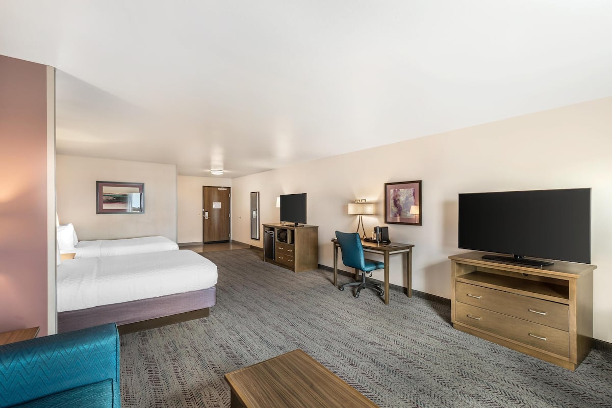A hotel room with a bed, desk, chair, television, and a small table.