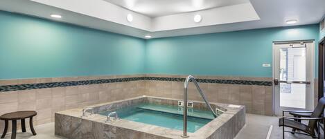 Un espace piscine intérieur moderne, doté d’une piscine rectangulaire, de marches permettant d’y accéder et de coins salon.