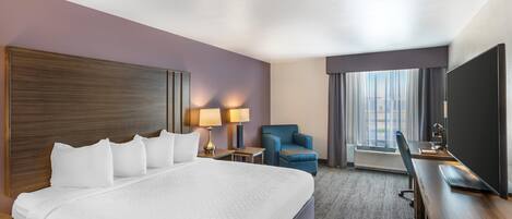Habitación de hotel con una cama grande, un escritorio con computadora, una silla y un televisor.