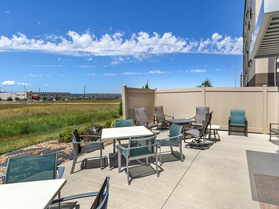 An outdoor patio with tables and chairs, a view of a field, and a building in the background.