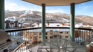A balcony with a grill and a table, overlooking a snowy mountain landscape with buildings.