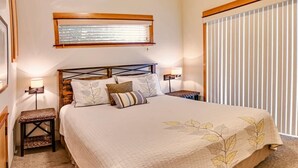 Quarto com uma cama grande, mesa de cabeceira, luminária na parede e janela com persianas.