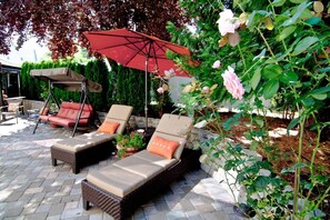 A patio area with two cushioned chairs and a swing chair, a red umbrella, and a climbing rose bush. - Lori Lanes 'juliet Cottage' ~ 2 Bedroom ~ Downtown (Ashland)