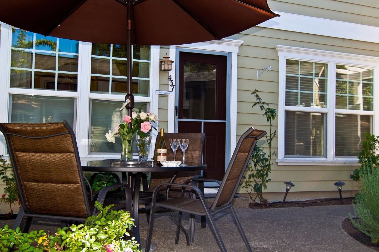 Eine Terrasse im Freien mit Tisch, Stühlen, einer Weinflasche und einem Blumenstrauß.