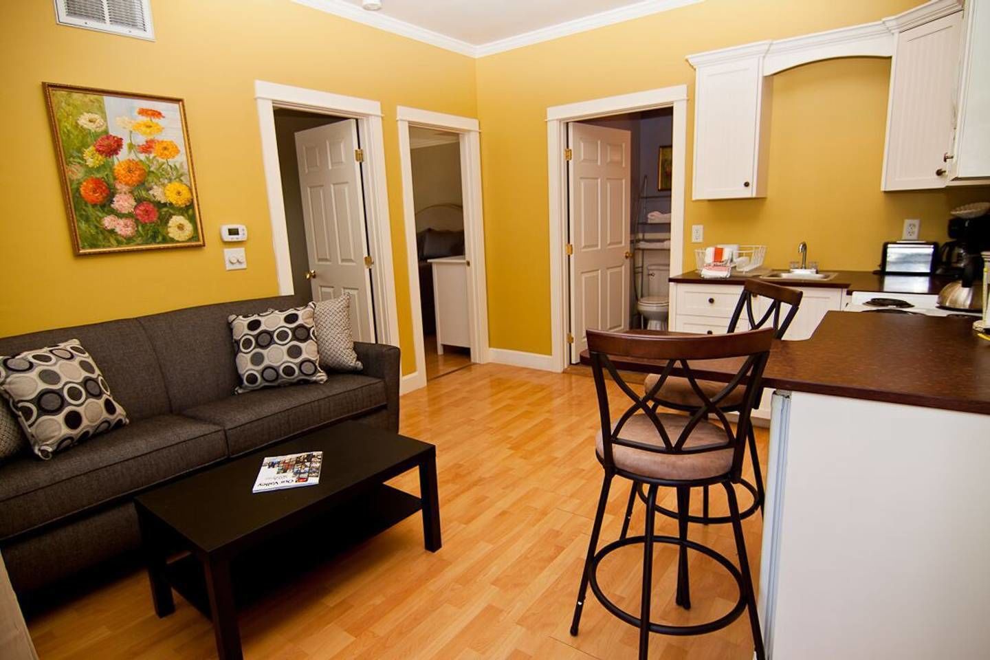 Un espacio habitable compacto con un sofá, una mesa de centro, una zona de cocina con una mesa de comedor y sillas, y un cuadro en la pared.