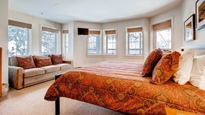 A bedroom with a large bed, a sofa, and multiple windows. - Centennial 2 Bedroom Condo Unit no. 7 (Avon)